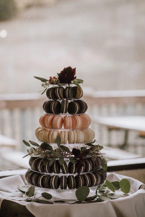 macaroon tower with floral accents including eucalyptus and red roses and hypericum berries