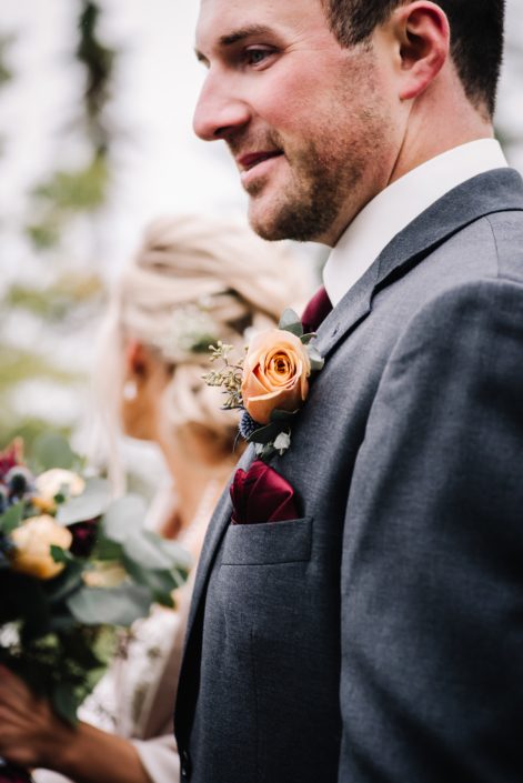 Groom wearing a grey suit and boutonierre designed with a mustard yellow rose and eucalyptus