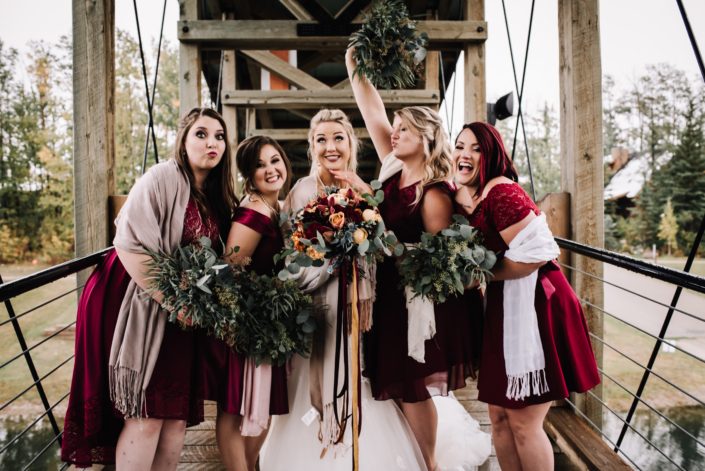 Bride and bridesmaids in burgundy short dresses with white shawls and eucalyptus greenery bouquets bride has a bouquet with silk trailing ribbons in burgundy, navy and mustard yellow and flowers in mustard yellow and burnt orange