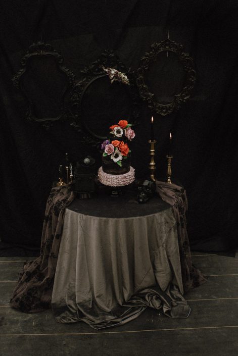 black backdrop for wedding cake with grey tablecloth and sugar flowers with red roses and mauve roses and white anemone