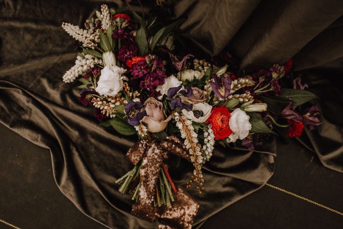 alternative bridal bouquet with red ranunculus and white anemone and white pieris and purple clematis and white lisianthus with a copper sequin handle wrap