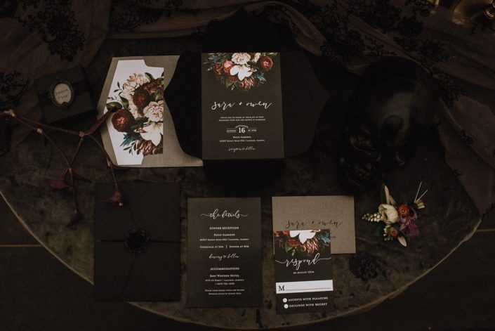 flat lay of black wedding invitations for alternative brides and grooms black skull and grey velvet and dark and moody