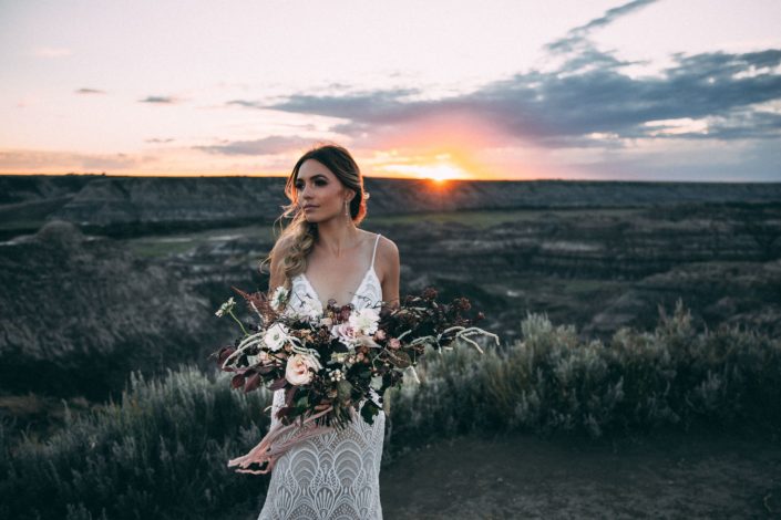 sunset photoshoot in drumheller with bride holding a boho sytle bridal bouquet designed with roses, scabiosa, and amaranthus with silk trailing ribbons