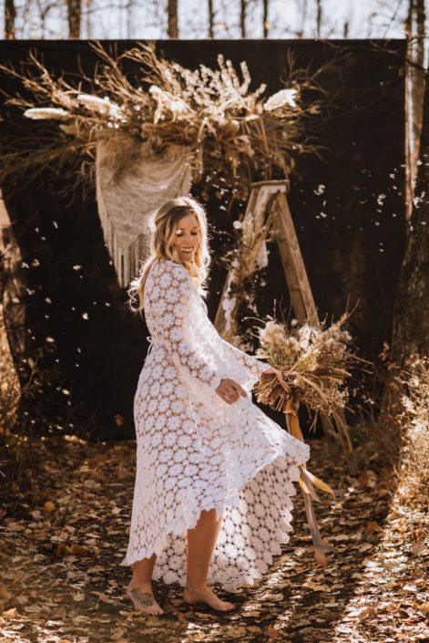 playful sunlit barefoot boho bride with crochet dress in fall with bouquet of dried florals with pampas grass and dried floral backdrop with crochet hanging