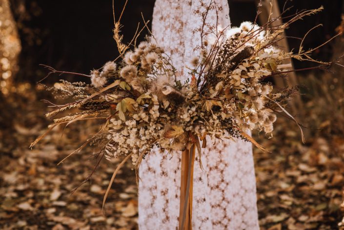 Fall boho bridal bouquet made with dried florals and trailing silk ribbons with lace dress