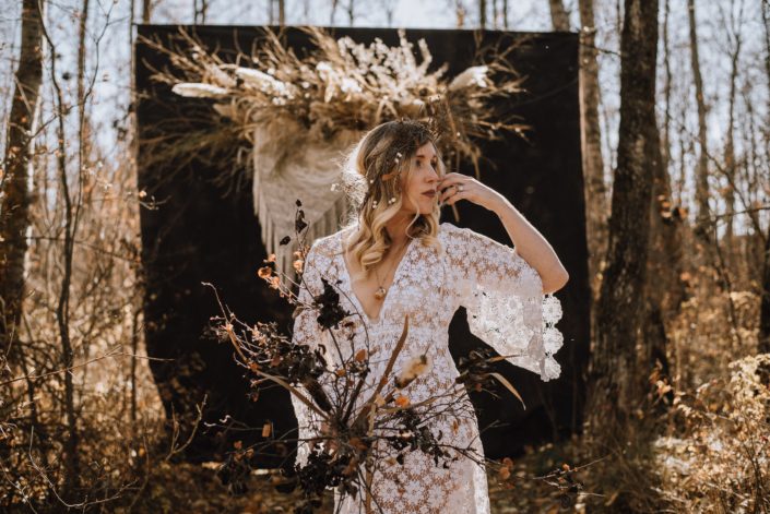 Fall boho bride with lace dress in the wood with dried pampas grass hanging with crochet and twig and a boho floral headdress