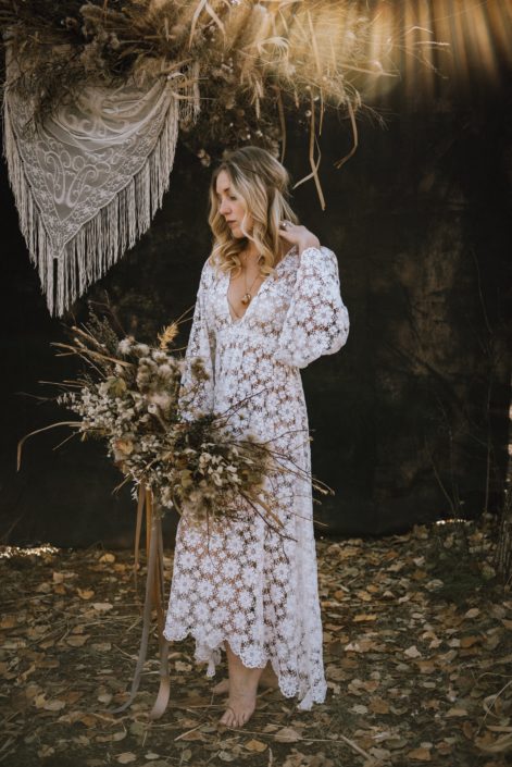 sunburst boho bride in the fall in the woods barefoot with a foraged bouquet made of dried dandelions and twigs ad fall toned trailing ribbons