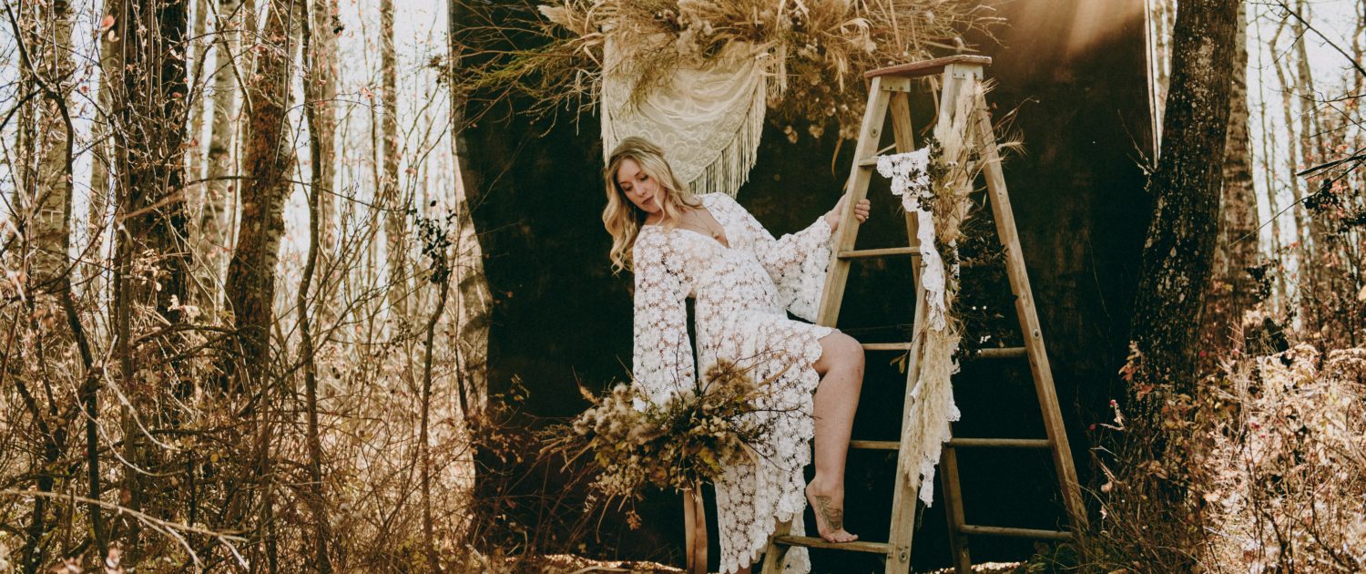 fall boho bride in crochet dress in the woods with dried pampas grass and dried floral backdrop and bouquet made of thistle and twig foraged from the woods