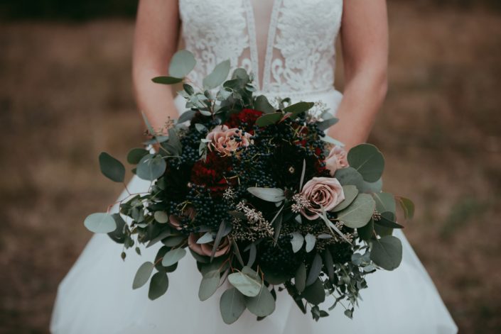 bouquet shot close up of bride bouquet with amnesia roses, viburnum berries in navy red roses and burgundy dahlias and mixed eucalyptus greenery bride gown with plunging neck and lace