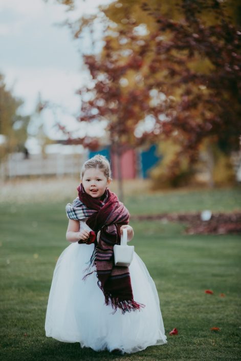 Fall wedding with flowergirl with plaid shawl walking down aisle with basket of red rose petals