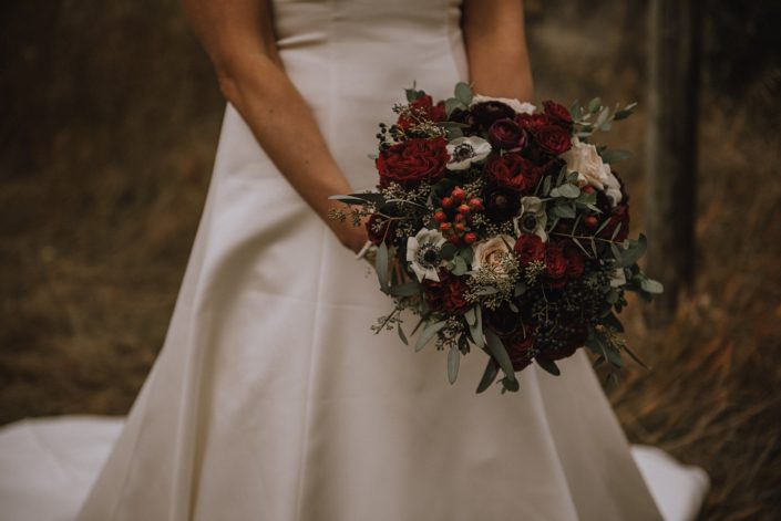 Elegant bride holding a bouquet designed with hypericum berries, hearts garden roses, panda anemone, burgundy ranunculus and eucalyptus