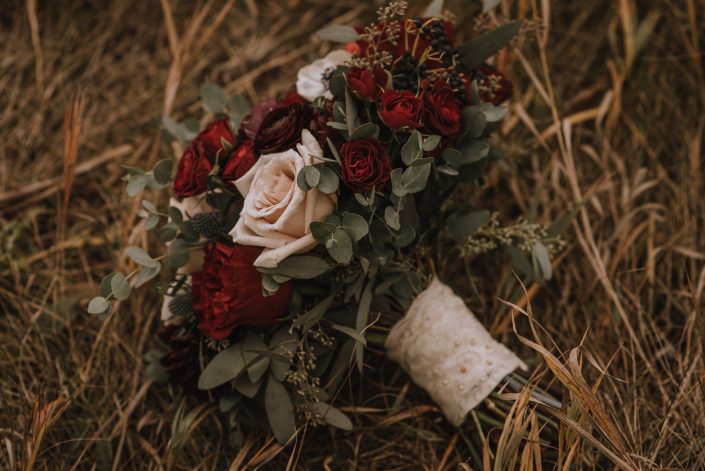 bridal bouquet designed with hearts garlden roses, burgundy ranunculus red spray roses eryngium and mixed euclayptus greenery, wrapped with ivory lace