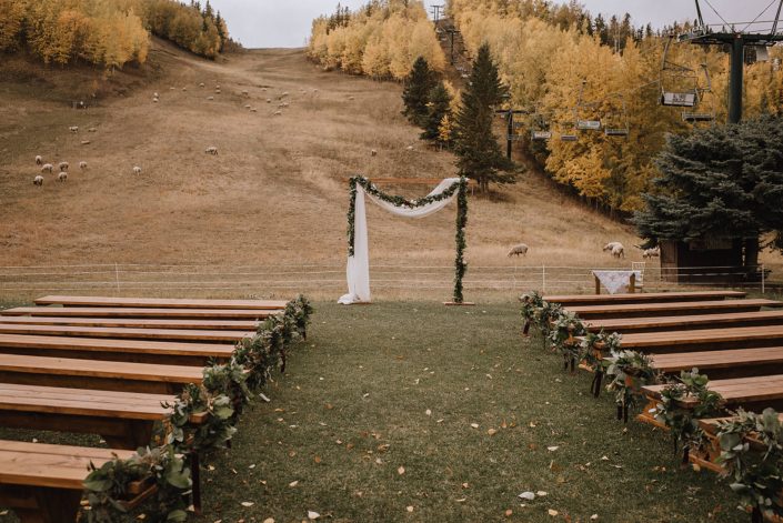 Eucalyptus rings used as ails markers n rustic benches for a ceremony at Canyon Ski Resort with a draped fabric and garland archway