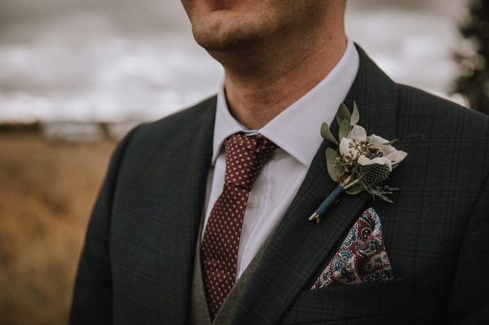 Groom with panda anemone and anenome boutonniere wrapped with navy silk ribbon