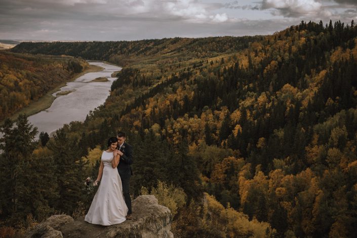 bride and groom wedding photos at Canyon Ski Resort overlooking the red deer river with burgundy and navy bridal bouquet