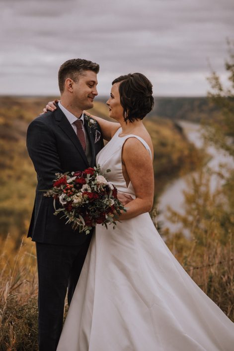 bride and groom at canyon ski resort overlooking the red deer river holding a burgundy and navy bridal bouquet
