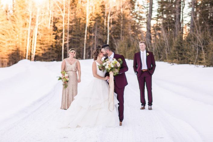 Winter wedding party with bride, bridesmaid, groom and groomsmen in Burgundy suits and blush sequin dress with bridal bouquet of burgundy helleborus, blush ranunculus, heleborus and white ranunculus