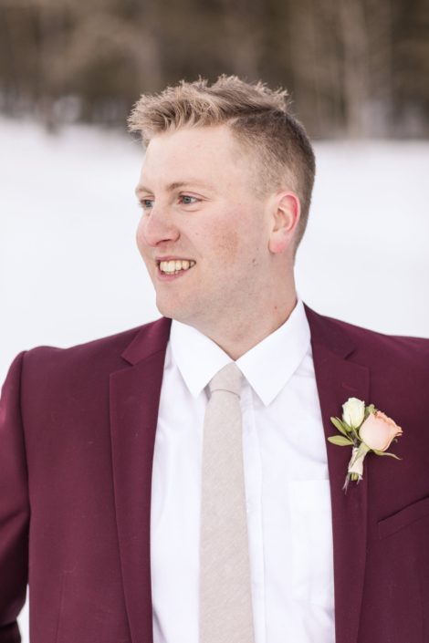 Winter Groom in burgundy suit with a pale peach spray rose boutonniere