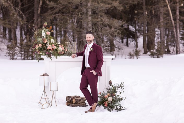Winter weddig styled shoot with groom in burgudy suit and mantle floral arrangements in peach and burgundy