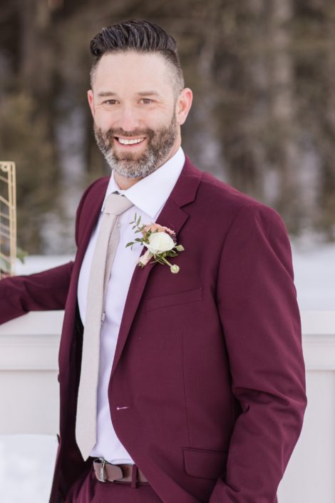 winter groom in a burgundy suit with ivory ranunculus boutonierre