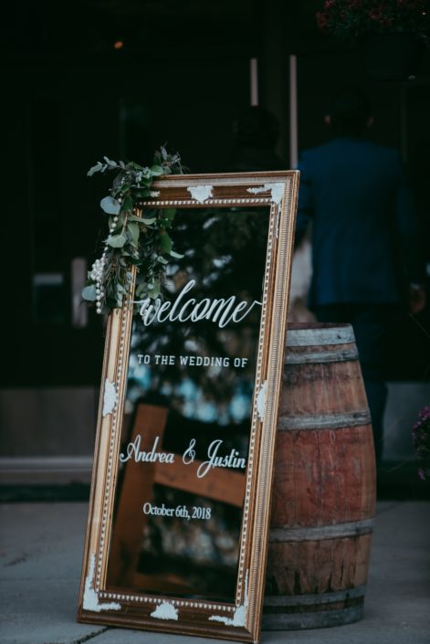Mirrored sign with gold frame and mixed eucalyptus garland with floral accents and a rustic barrel