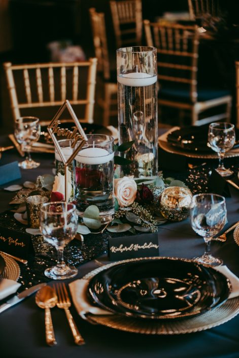 Art deco style dark and moody wedding centerpiece of clear cylenders with candles and fresh mixed eucalyptus greenery and roses at the base