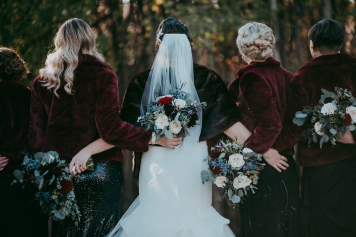 Fall bridal party picture from behind with fur coats and black sequin dresses bouquets with red roses quicksand roses eryngium and mixed eucalyptus retro bridal party
