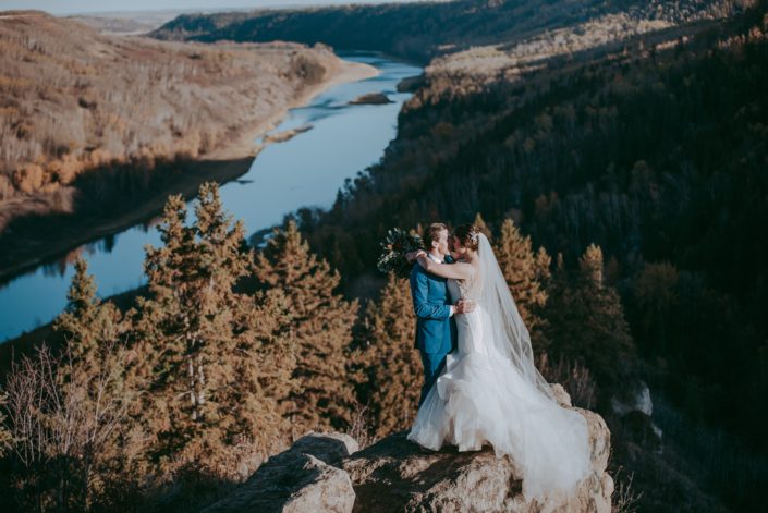 Beautiful river valley view wedding photo of bride and groom in fall with long veil and groom in a blue suit