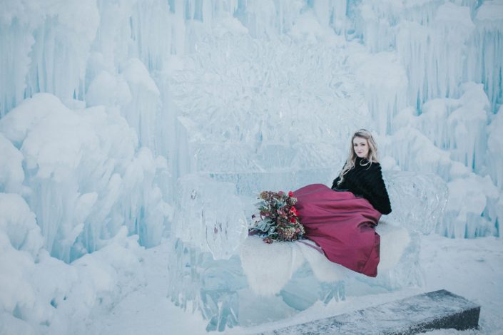 Bride sitting on ice couch at the edmonton ice castles with burgundy bouquet