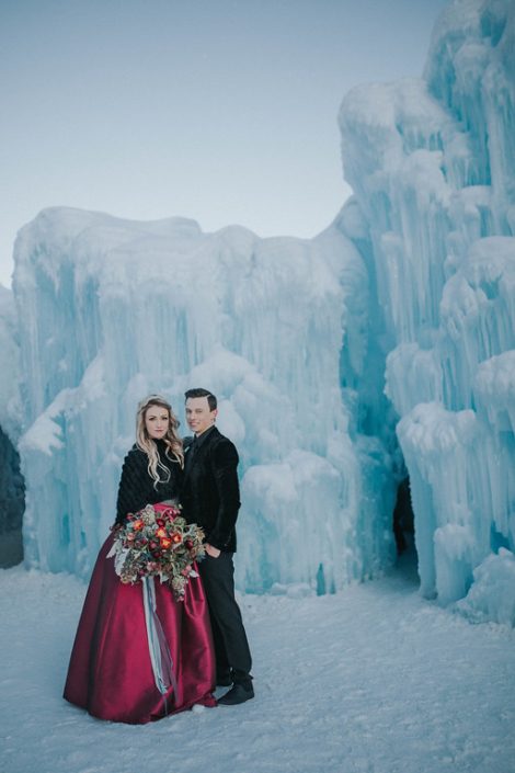 a styled engagement photoshoot at the edmonton alberta ice castles with the bride holding a bouquet of burgundy frittilaria, red helleborus and red tulips