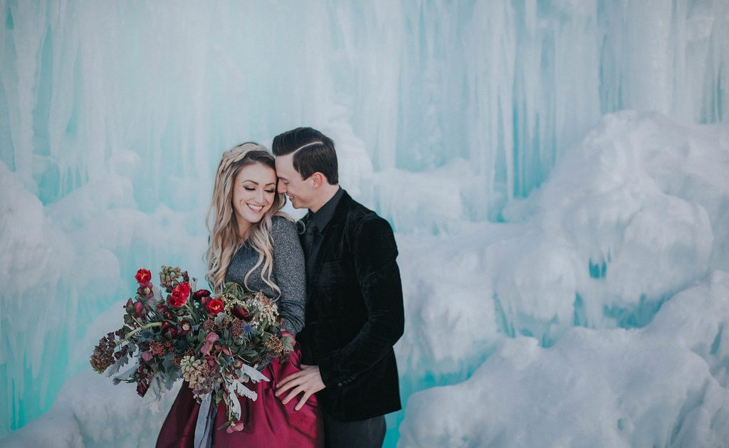 Bride and Grooms smiling for their engagement photoshoot at the ice castles in winter in edmonton alberta with a bridal bouquet of tulips, frittilaria and helleborus