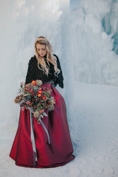 A styled engagement shoot at the edomton ice castles with a black fur shawl, and a bouquet made with red tulips, burgundy frittilaria and burgundy ranunculus