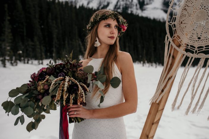 Boho bride in the winter with macrame backdrop and eucalyptus and burgundy bouquet wearing a greenery flowercrown