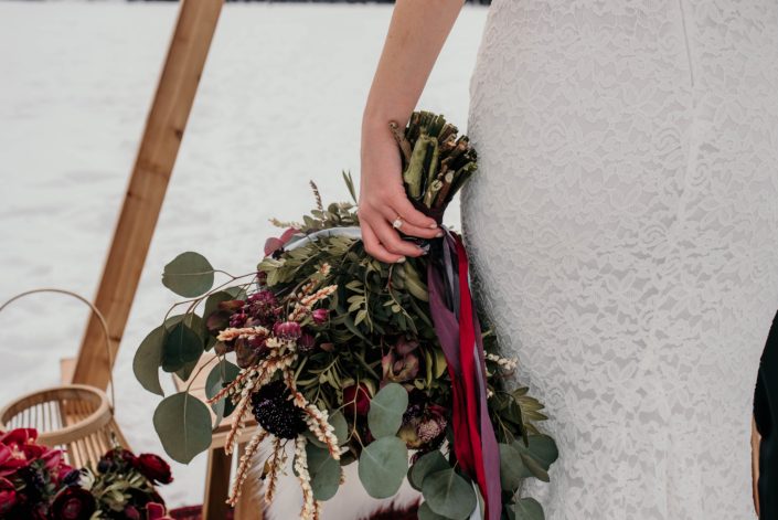 bride with engagement ring holding a loose and natural greenery bouquet tied with trailing silk ribbons