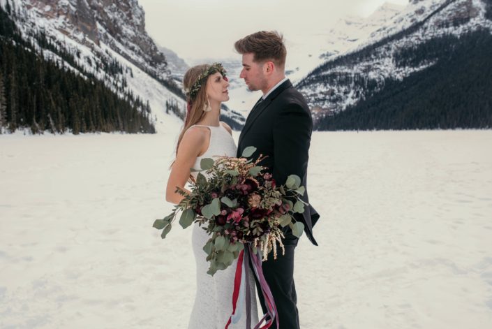 bride and groom in lake louise with organic greenery and burgundy bridal bouquet
