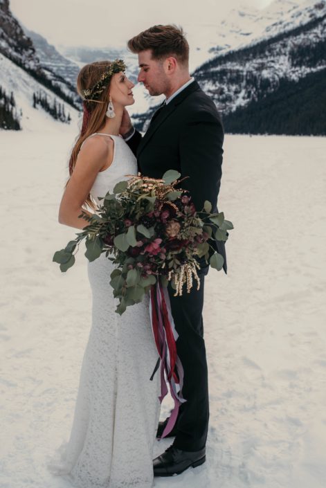 bride and groom at lake louise alberta with eucalyptus greenery bouquet and burgundy orchids