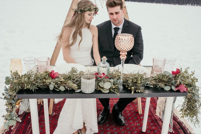 winter photoshoot at lake louise with a greenery garland with burgundy accents placed along the sweetheart table