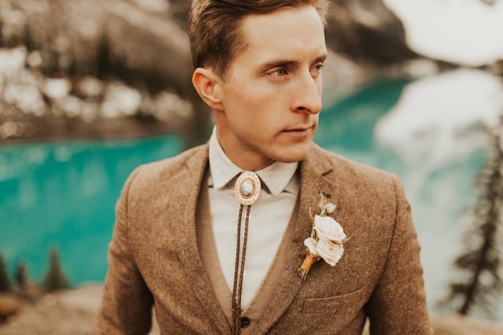 Moraine Lake Elopement Styled Shoot - male model wearing ivory boutonniere, brown jacket and bolo tie