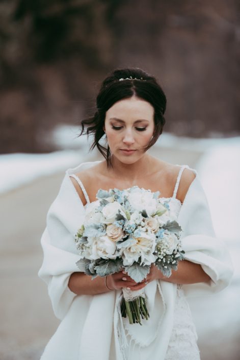 Winter bride with compact hand tied bouquet of white peony, ivory roses and delphinium