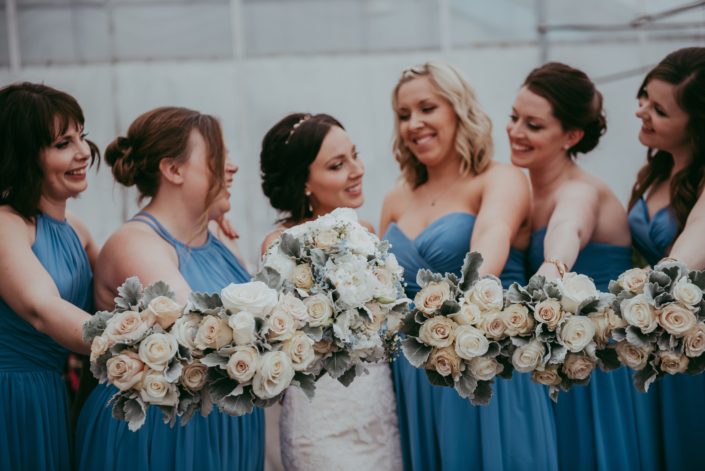 Bride and bridesmaids in sky blue holding bouquets of pale peach and ivory roses with grey dusty miller