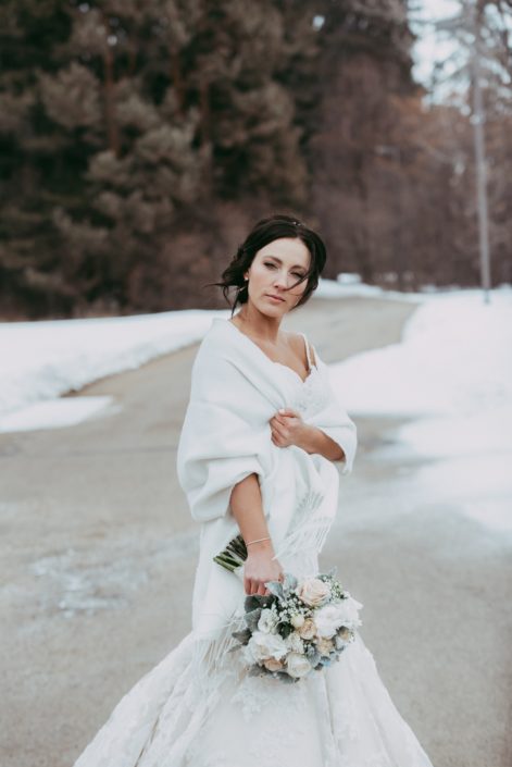 Bride in winter with a white shawl and bridal bouquet of white peony and ivory roses
