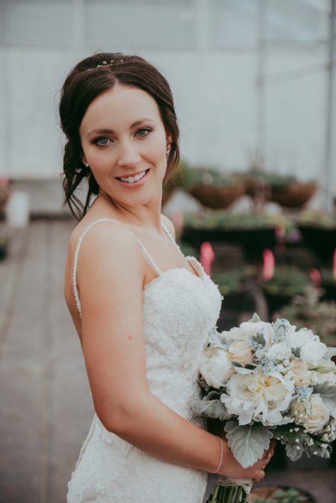 bride in a wedding dres holding a bouquet with white peonies, ivory roses, dusty miller and pale blue delphinium