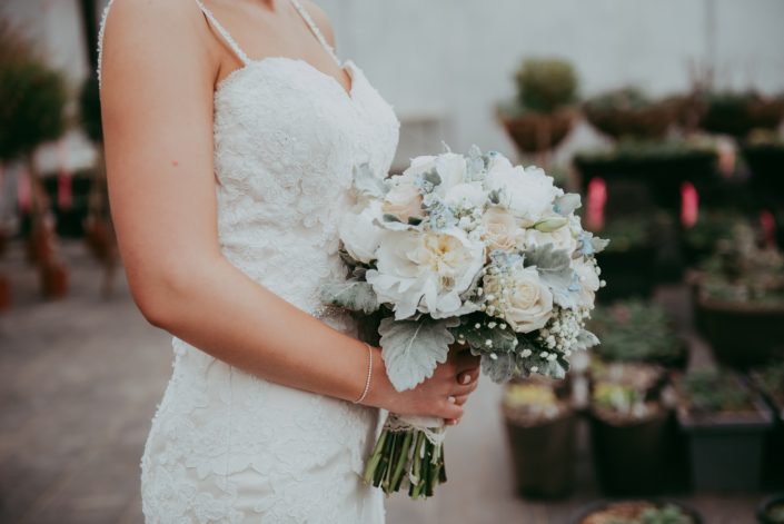 bride holding a bouquet of white peonies, ivory roses and pale blue delphinium with babies breath