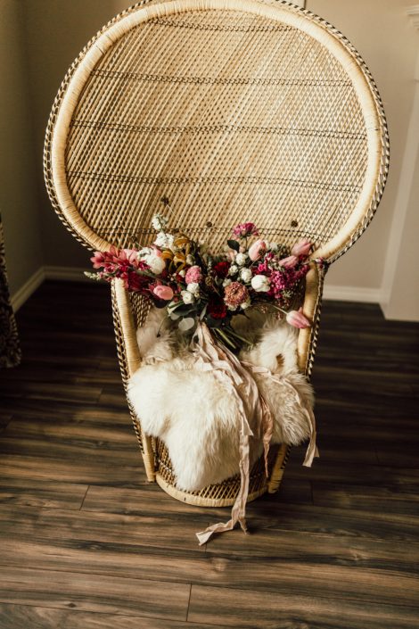 Red and Pink Styled Shoot - bouquet made of pink and white tulips, scabiosa, roses, and greenery tied with trailing ribbon. It is atop a vintage boho rattan chair covered in a sheepskin rug.