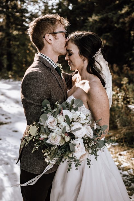 Groom kissing bride holding a white and blush bouquet with roses and eucalyptus