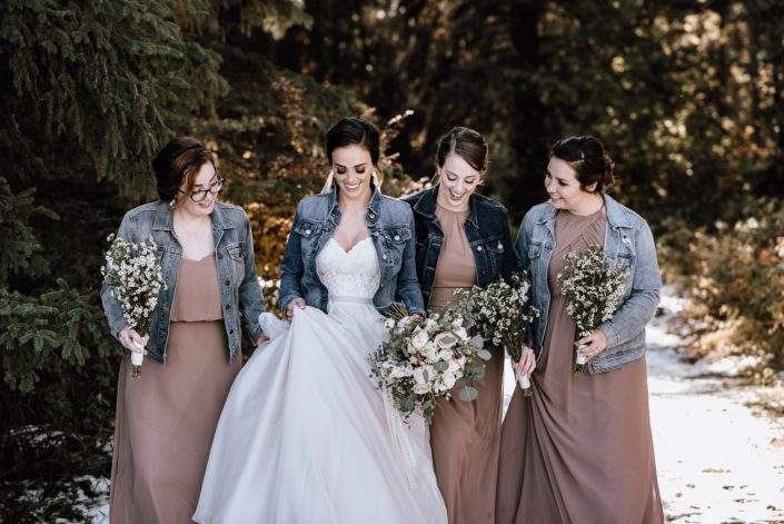 bride and bridesmaids in jean jackets and dusty rose dresses with white rose and waxflower bouquets