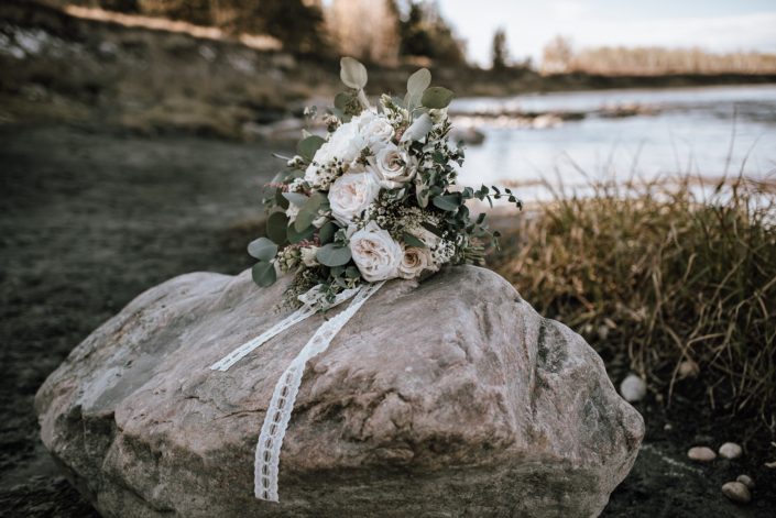 Bride's bouquet on a rock in the fall designed with white and blush roses and eucalyptus
