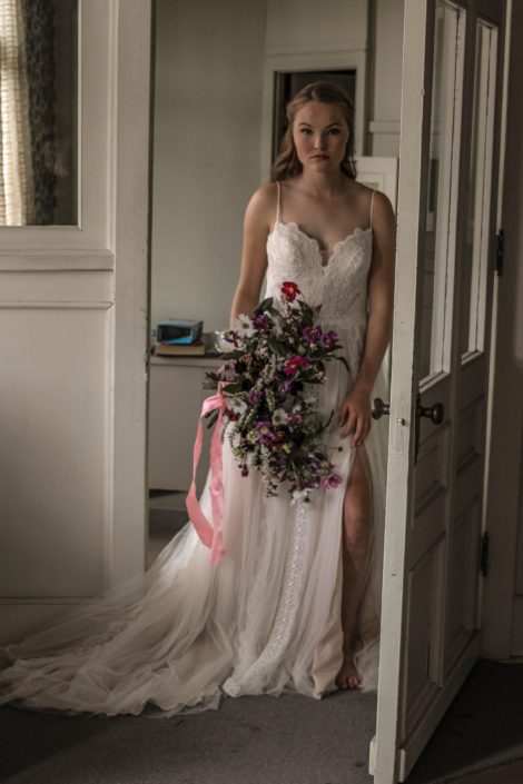 Pink Vintage Photoshoot - model wearing ivory bridal gown and veil holding white, pink and purple wildflower bouquet made of cosmos and greenery tied with trailing ribbons.