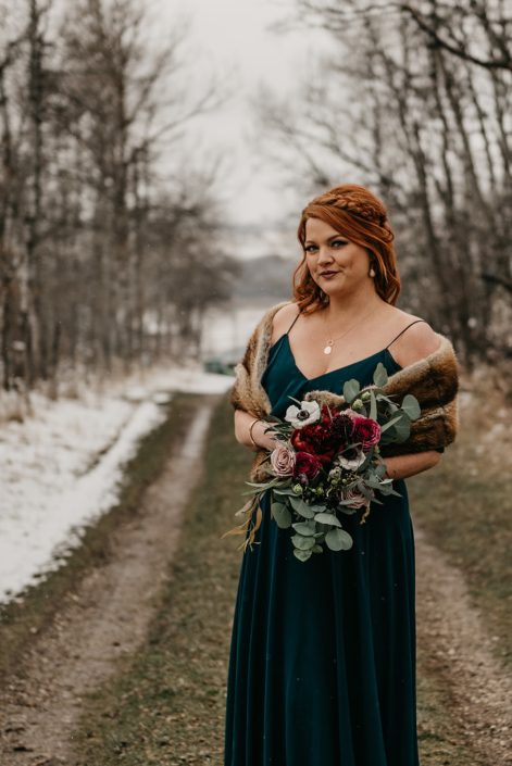 Rustic Boho Chic Wedding - Bridesmaid wearing emerald green dress and fur shawl off the shoulders while holding a bouquet made of red peony, blush and pink roses, and eucalyptus greenery.