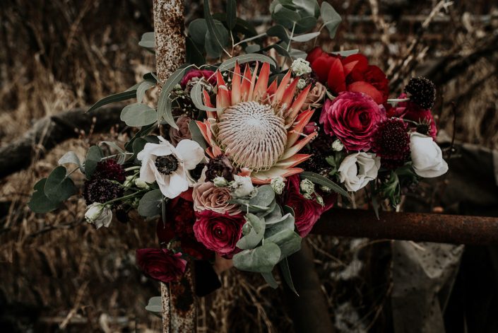 Rustic Boho Chic Wedding - Bridal bouquet made of king protea, red peonies, pink roses, plum scabiosa, panda anenome, and eucalyptus greenery.